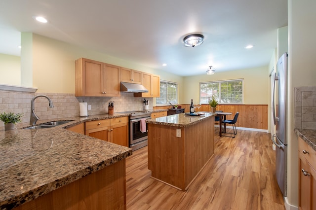 kitchen featuring appliances with stainless steel finishes, stone countertops, sink, a center island, and light hardwood / wood-style flooring