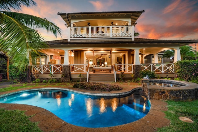 back house at dusk featuring a pool with hot tub, ceiling fan, a patio, and a balcony