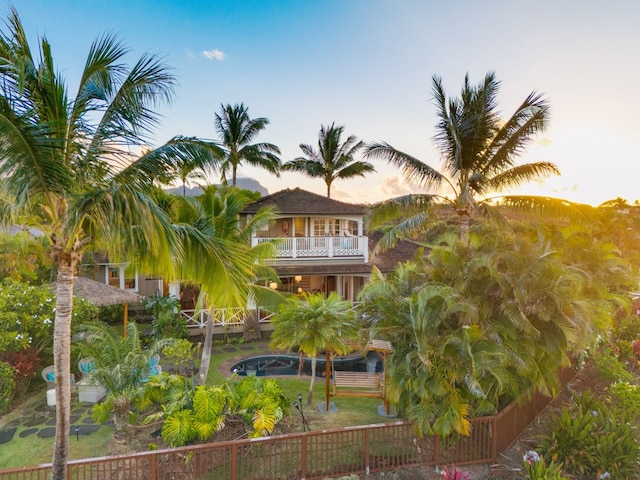 back house at dusk featuring a fenced in pool and a balcony