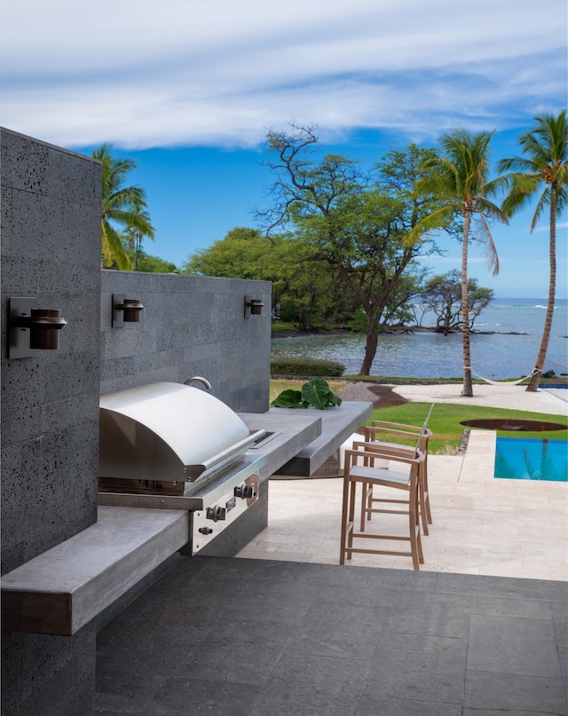 view of patio with grilling area, a water view, and an outdoor kitchen