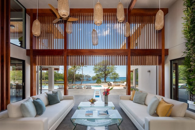 living room featuring a water view, ceiling fan, and a towering ceiling