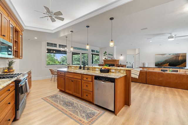 kitchen with light stone countertops, stainless steel appliances, hanging light fixtures, and light hardwood / wood-style flooring