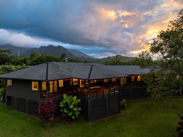 back house at dusk featuring a deck with mountain view and a lawn