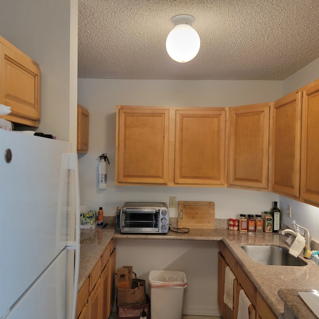 kitchen featuring sink, white fridge, light stone countertops, and a textured ceiling