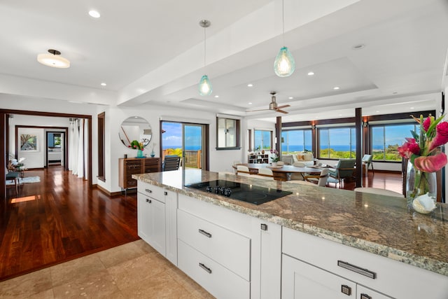 kitchen with light stone countertops, black electric cooktop, white cabinets, decorative light fixtures, and a tray ceiling