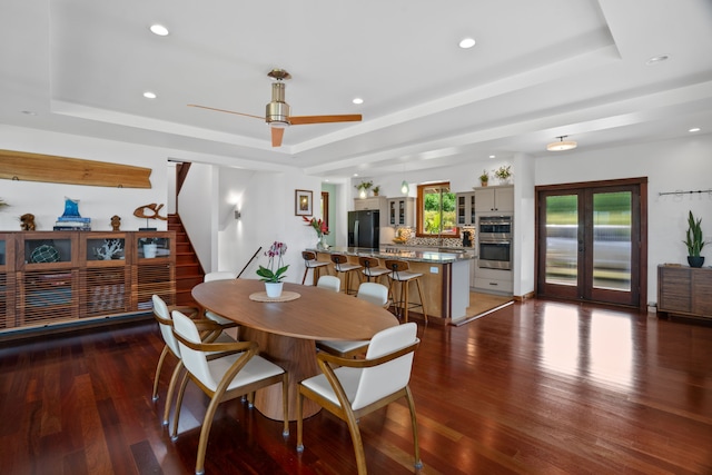 dining area featuring dark wood-type flooring, ceiling fan, and a raised ceiling