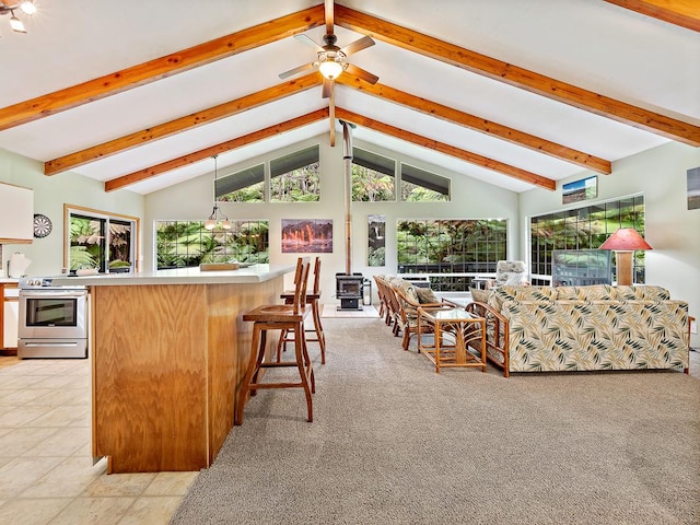 interior space with ceiling fan, light colored carpet, beamed ceiling, and a wood stove