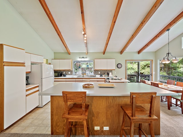 kitchen with a breakfast bar area, light colored carpet, white refrigerator, lofted ceiling with beams, and a center island with sink