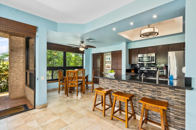 kitchen featuring appliances with stainless steel finishes, a raised ceiling, a wealth of natural light, and dark brown cabinets