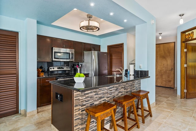 kitchen featuring decorative backsplash, a kitchen bar, sink, kitchen peninsula, and stainless steel appliances