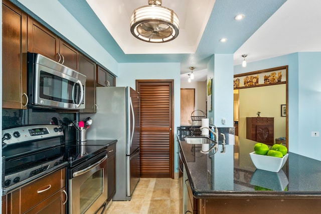 kitchen featuring a raised ceiling, light tile patterned floors, dark stone countertops, kitchen peninsula, and stainless steel appliances