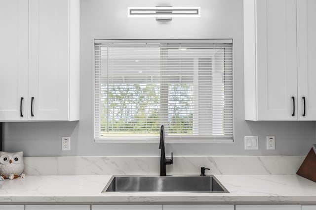 kitchen with white cabinetry, light stone countertops, and sink