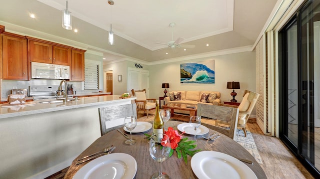 dining space with light wood-type flooring, ornamental molding, sink, and a tray ceiling