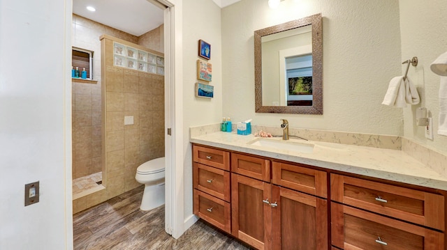 bathroom featuring tiled shower, hardwood / wood-style floors, vanity, and toilet