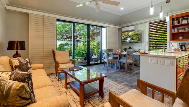 living room featuring ceiling fan, sink, a wall unit AC, hardwood / wood-style floors, and ornamental molding