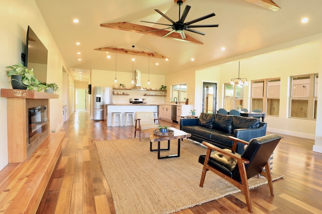 living room with beamed ceiling, ceiling fan with notable chandelier, high vaulted ceiling, and light hardwood / wood-style floors