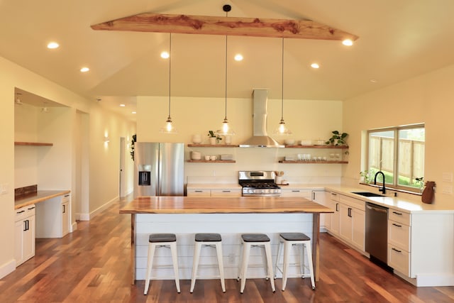 kitchen with appliances with stainless steel finishes, lofted ceiling with beams, a kitchen island, wall chimney range hood, and white cabinets