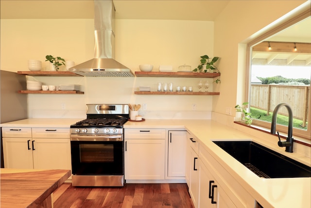 kitchen featuring wall chimney range hood, dark wood-type flooring, white cabinets, gas range, and sink