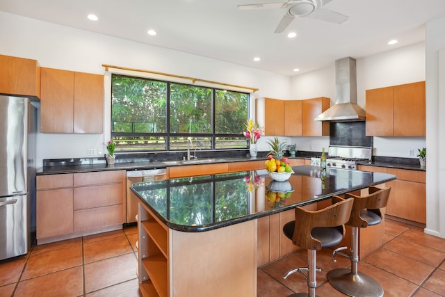 kitchen with stainless steel appliances, wall chimney exhaust hood, sink, a center island, and ceiling fan