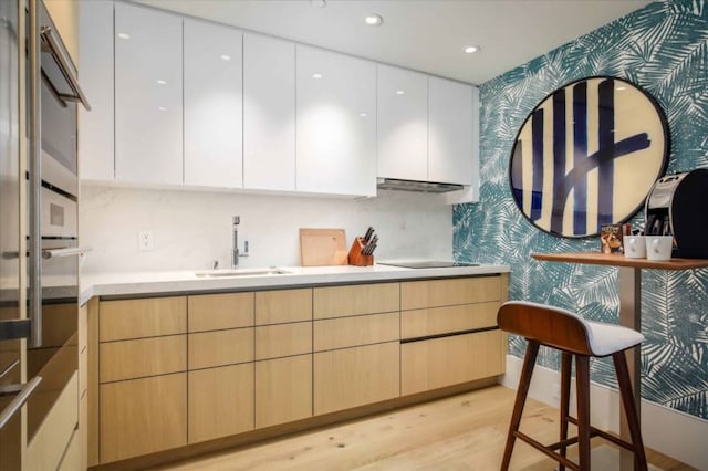 kitchen featuring white cabinetry, light hardwood / wood-style floors, black electric cooktop, and sink