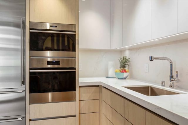 kitchen featuring light brown cabinetry, sink, light stone countertops, appliances with stainless steel finishes, and backsplash