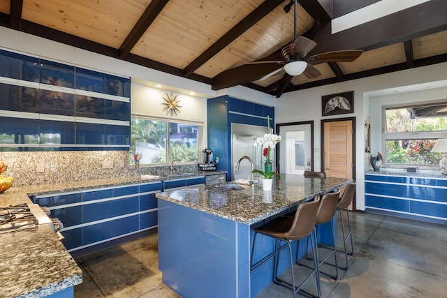 kitchen with blue cabinets, stone countertops, a kitchen island with sink, and a wealth of natural light