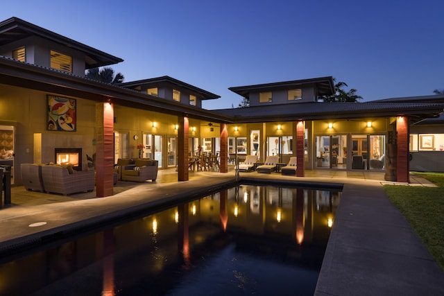 pool at dusk with a patio and an outdoor living space with a fireplace