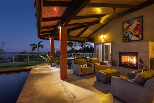 patio terrace at dusk featuring ceiling fan and an outdoor living space with a fireplace