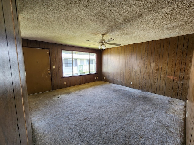 unfurnished room with a textured ceiling, wood walls, carpet floors, and ceiling fan