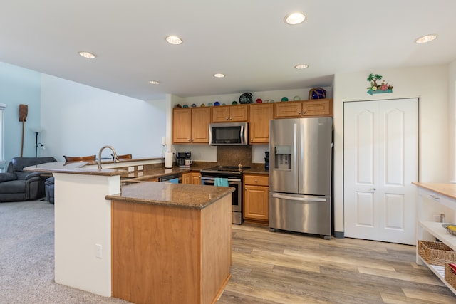 kitchen featuring kitchen peninsula, stainless steel appliances, decorative backsplash, light carpet, and sink