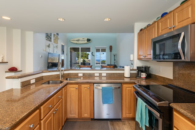 kitchen with appliances with stainless steel finishes, sink, kitchen peninsula, decorative backsplash, and dark wood-type flooring