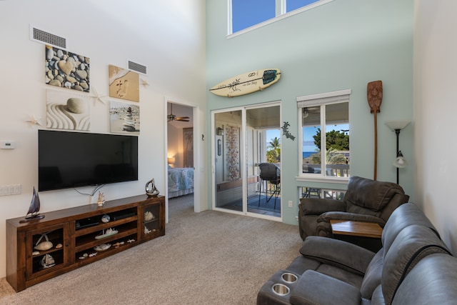 living room with carpet floors, ceiling fan, and a towering ceiling