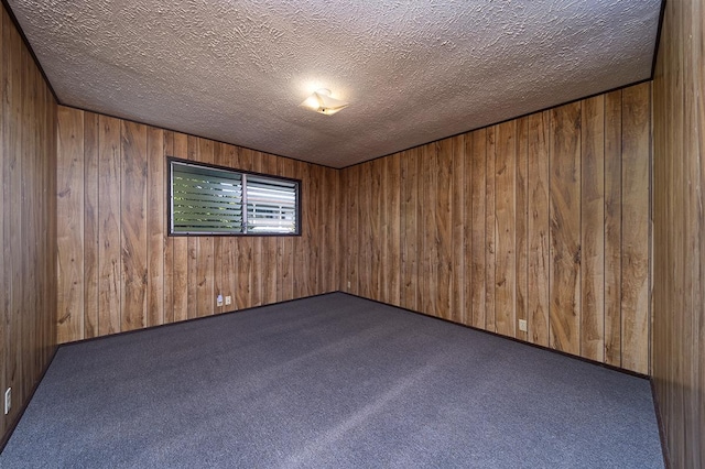 unfurnished room featuring a textured ceiling, dark carpet, and wood walls