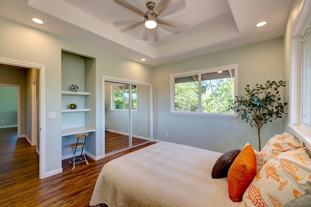 bedroom featuring a closet, a tray ceiling, dark wood-type flooring, and ceiling fan