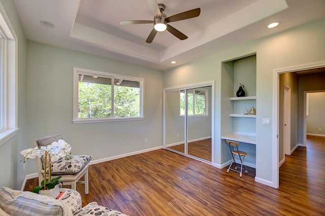 sitting room featuring ceiling fan, dark hardwood / wood-style floors, built in shelves, and a tray ceiling