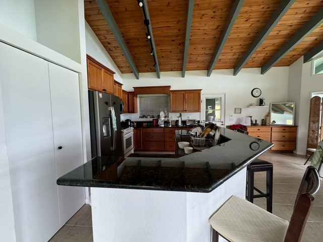 kitchen with tile patterned floors, track lighting, stainless steel fridge with ice dispenser, a breakfast bar, and wood ceiling