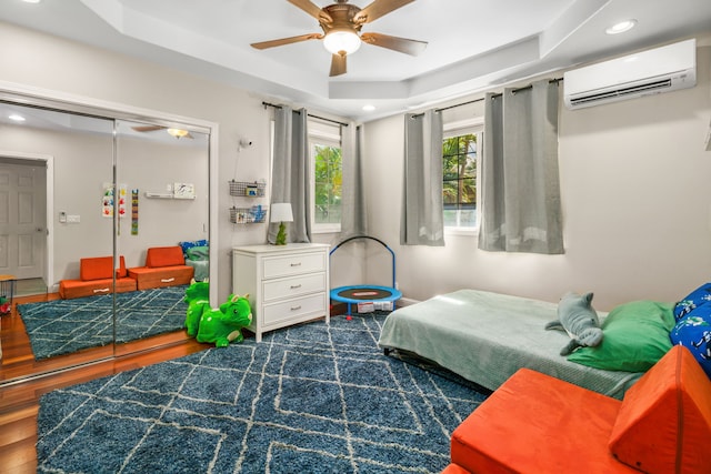 bedroom featuring ceiling fan, a raised ceiling, dark hardwood / wood-style floors, a closet, and a wall mounted AC