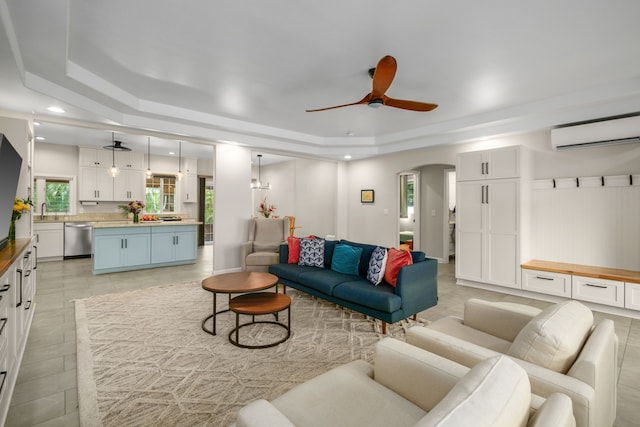 living room featuring ceiling fan, a tray ceiling, light tile patterned flooring, and a wall mounted air conditioner