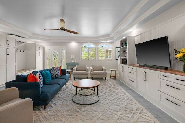 tiled living room featuring ceiling fan and a tray ceiling