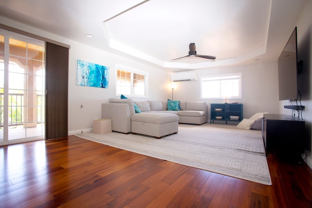 living room with a tray ceiling, an AC wall unit, ceiling fan, and wood-type flooring