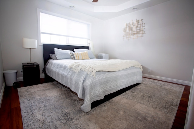 bedroom with a raised ceiling, ceiling fan with notable chandelier, and hardwood / wood-style floors