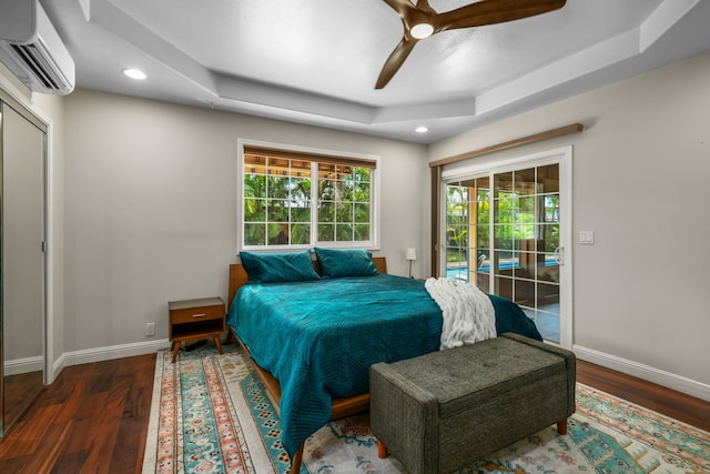 bedroom featuring a raised ceiling, access to exterior, wood-type flooring, a wall mounted air conditioner, and ceiling fan