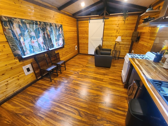 sitting room featuring lofted ceiling with beams, wooden walls, hardwood / wood-style floors, and a barn door