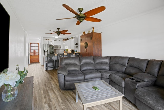 living room featuring light wood-type flooring, ceiling fan, ornamental molding, and a textured ceiling