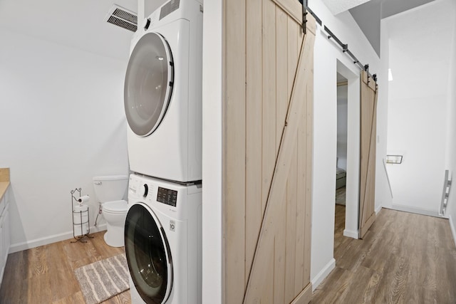 clothes washing area with stacked washer and clothes dryer, wood-type flooring, and a barn door