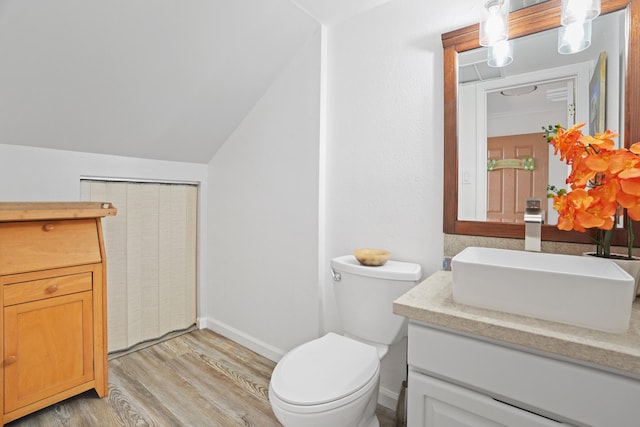 bathroom with toilet, hardwood / wood-style floors, vaulted ceiling, and vanity