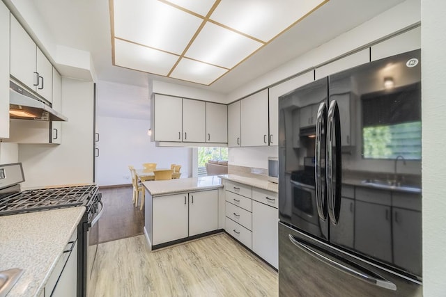 kitchen with light countertops, stainless steel gas range oven, freestanding refrigerator, and under cabinet range hood