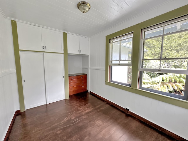 unfurnished bedroom with dark wood-type flooring, crown molding, and a closet