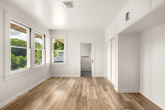 unfurnished bedroom with a closet, light wood-type flooring, and wooden walls