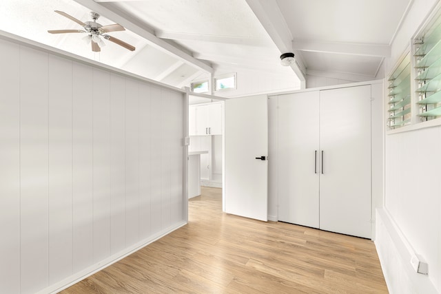 unfurnished bedroom with vaulted ceiling with beams, a closet, wooden walls, light hardwood / wood-style flooring, and ceiling fan